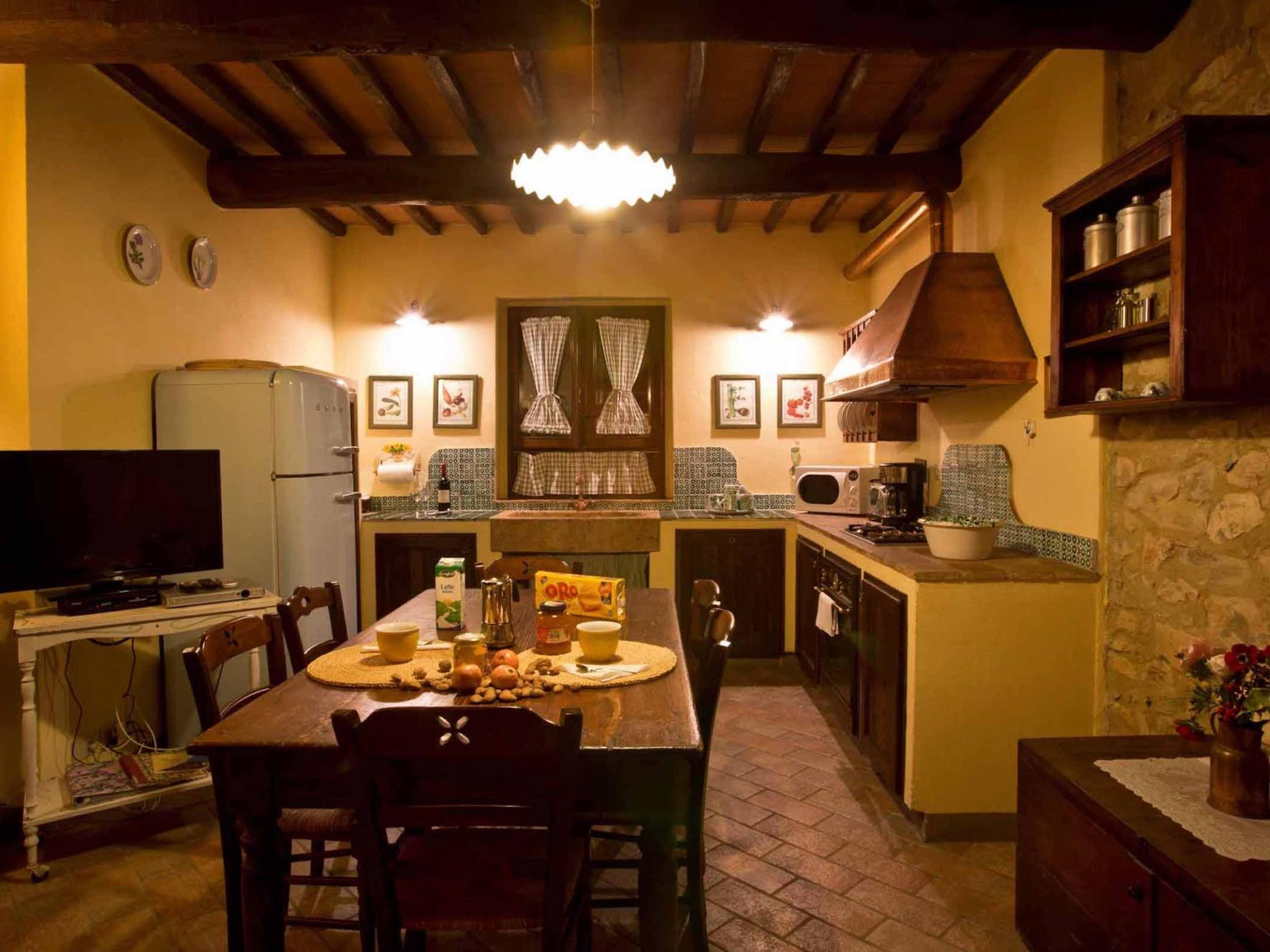 Una cocina acogedora con una mesa de madera, sillas, un televisor y un refrigerador.