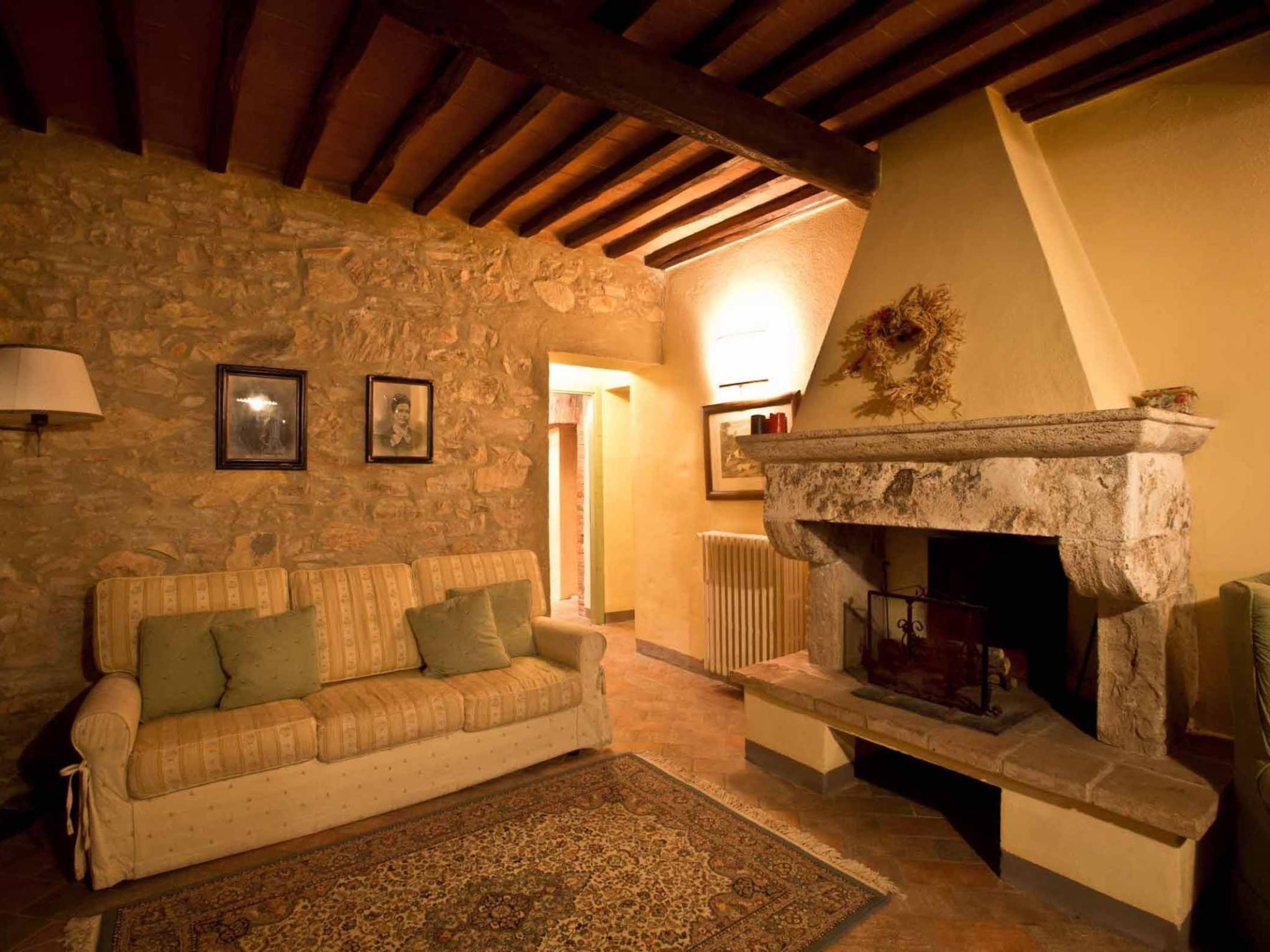 A cozy living room with a stone wall, a fireplace, a sofa, and a patterned rug.