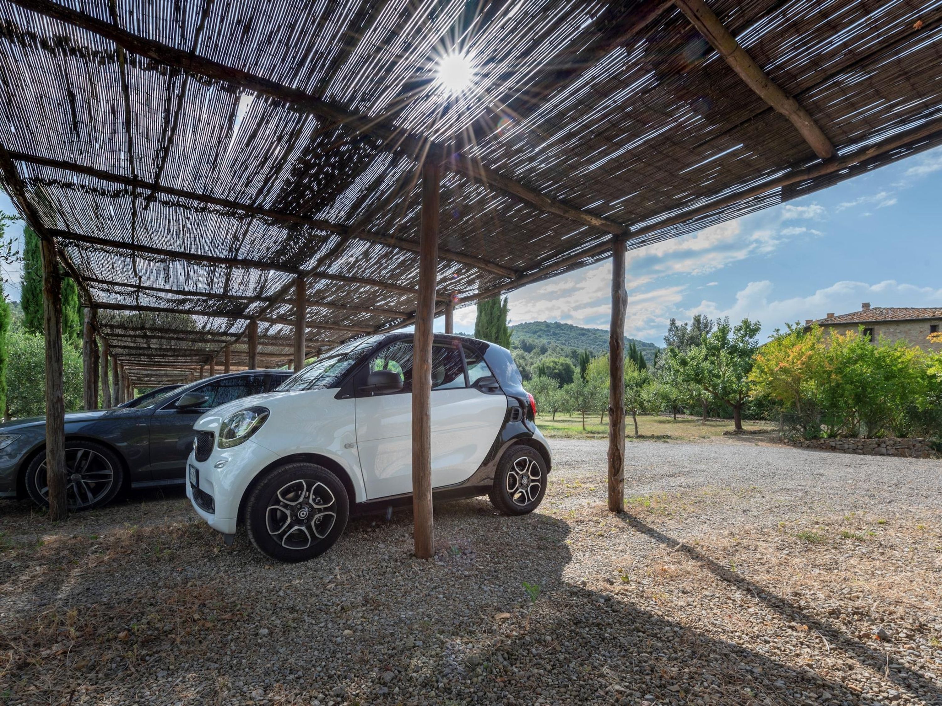 A white car parked under a covered area with a gravel ground.