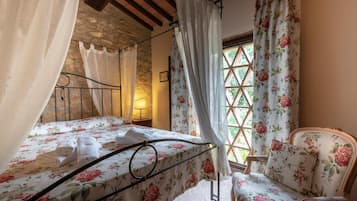 Ein Schlafzimmer mit Bett, Stuhl und einem Fenster mit blumigen Vorhängen.