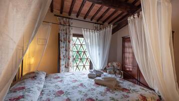 Un dormitorio con edredón estampado con motivos florales, cabecera de madera, ventana con diseño de celosía y armario de madera.