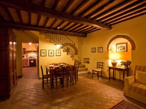 A dining area with a wooden table and chairs, a staircase, and a cozy seating area with a lamp.