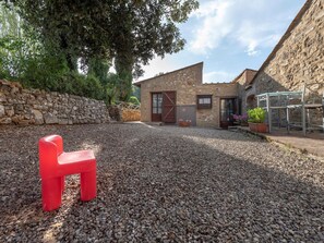 A stone building with a gravel courtyard, a red plastic chair, and potted plants.