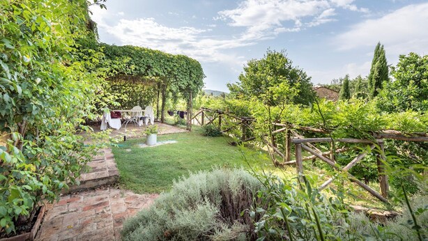A rustic garden with a brick pathway, a pergola covered in greenery, and a seating area with chairs and a table. - Apartment in Chianti With Pool ID 453 (Casole d'Elsa)