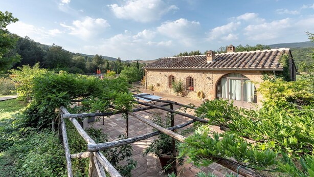 A stone building with a tiled roof, surrounded by lush greenery and a wooden pergola. - Country House a Casole d Elsa ID 451 (Casole d'Elsa)