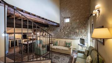 A rustic interior with a stone wall, a staircase, a sofa, and a television.