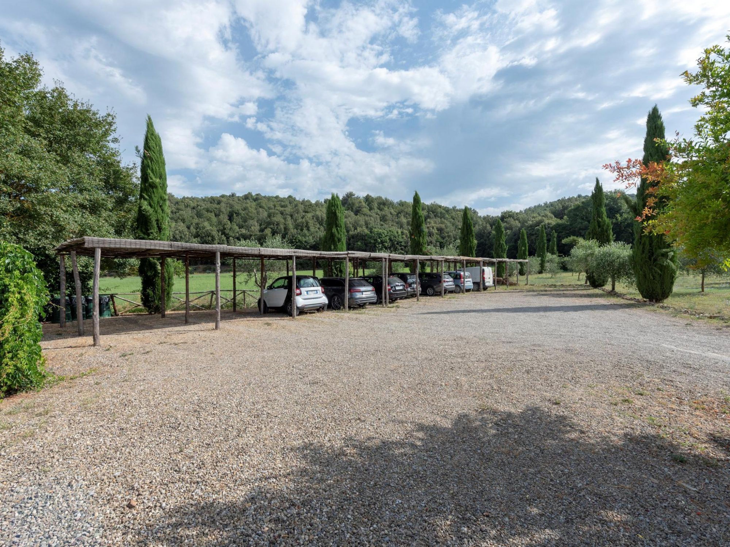 A gravel parking area with a covered car park and a row of parked cars.