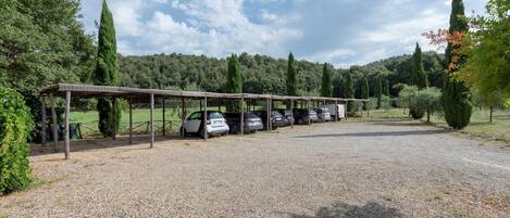 A gravel parking area with a covered car park and a row of parked cars.