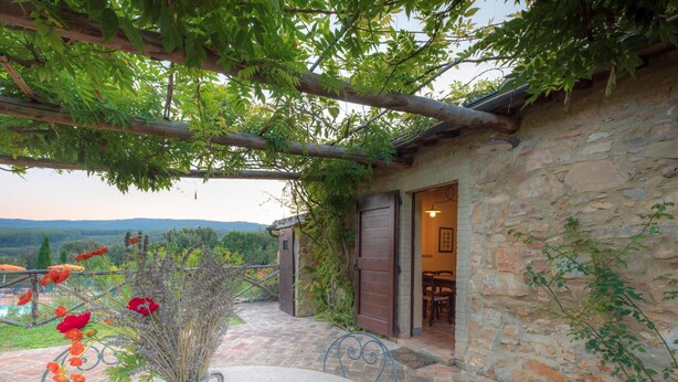 A stone building with a wooden door and a table with a vase of flowers. - Apartment in Chianti With Pool ID 455 (Casole d'Elsa)