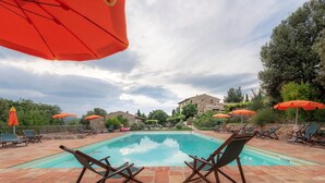A swimming pool with lounge chairs and orange umbrellas, surrounded by stone buildings and trees. - Apartment in Chianti With Pool ID 455 (Casole d'Elsa)