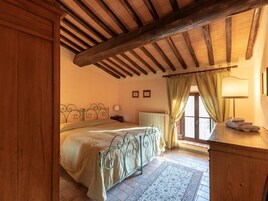 A bedroom with a bed, a nightstand, a radiator, a window with curtains, and a wooden ceiling.