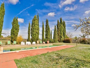 A pool area with tall cypress trees, a red brick pathway, and outdoor seating.