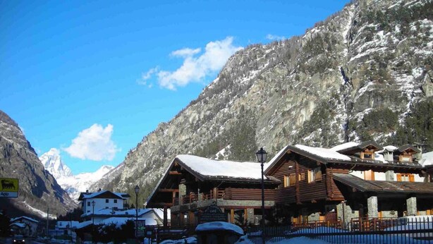 A mountain lodge with wooden cabins, a sign for a restaurant, and a view of snow-covered mountains. - Apartment La Gran Becca - ID 831 (Antey-Saint-Andre)