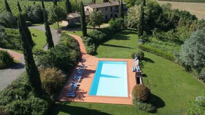 Vue aérienne d’une propriété dotée d’une piscine, de chaises longues et d’un grand bâtiment entouré de verdure.