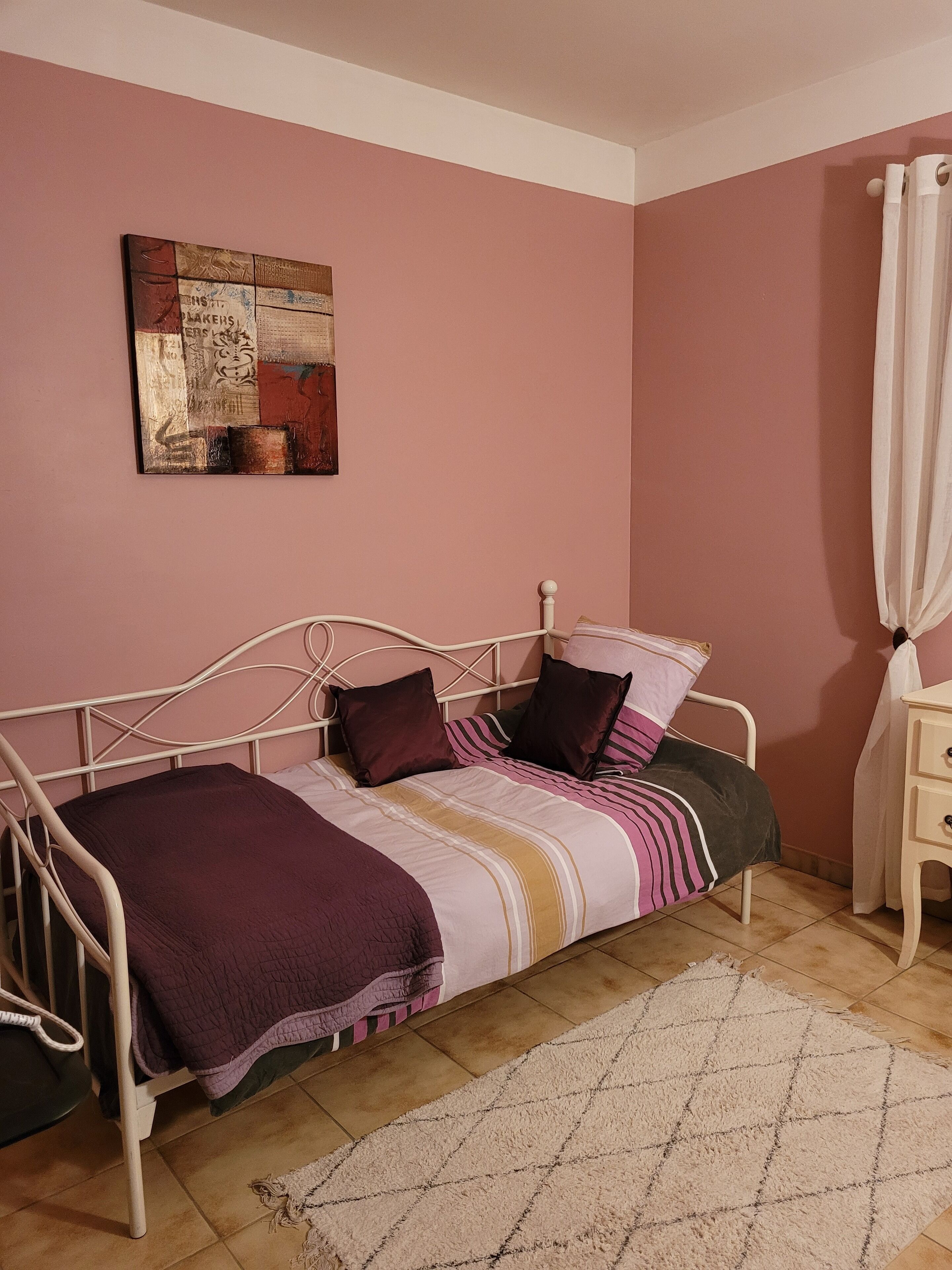 Une chambre à coucher avec un lit, une table de chevet, un tableau et un rideau.