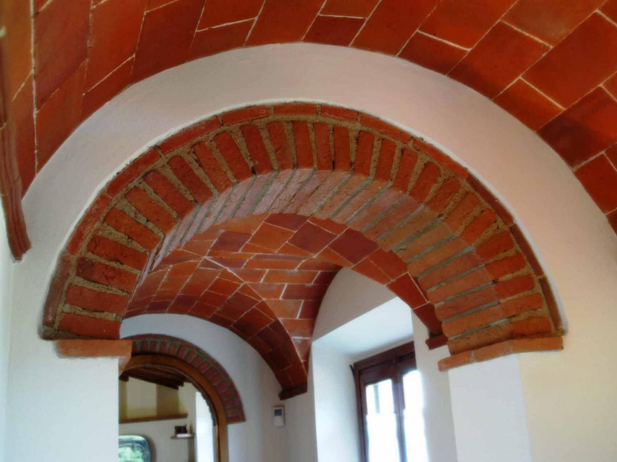 Eine gewölbte Ziegeldecke mit einer weißen Wand und einem Durchgang zu einem anderen Raum.
