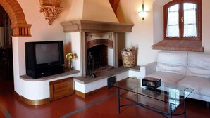 A living room with a fireplace, a television, a sofa, and a glass coffee table. - Country House in Chianti With Pool ID 33 (Montaione)