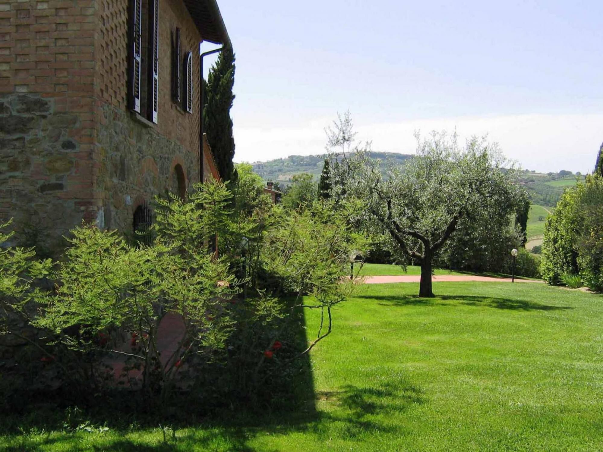 Un edificio in pietra con finestre ad arco e un prato curato con un grande albero al centro.