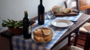 Ein Tisch mit karierter Tischdecke, eine Schale geröstetes Brot, eine Weinflasche, ein Glas, ein Laib Brot und ein Korb mit grünen Bohnen.
