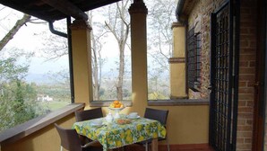 Un patio con una mesa preparada para dos, vistas a árboles y un paisaje lejano, además de un muro de ladrillo con una reja metálica.