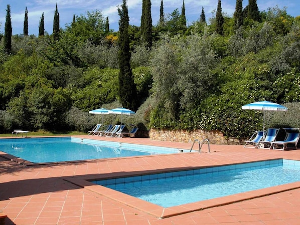 A swimming pool with lounge chairs and umbrellas, surrounded by trees and a stone wall.