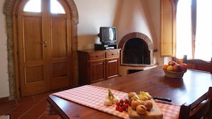 Eine rustikale Küche mit Kamin aus Stein, Holzschränken und einem Esstisch mit kariertem Tischläufer.