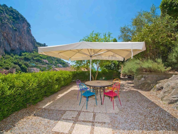An outdoor patio with a round table and colorful chairs, a large umbrella, and a scenic view of a mountainous area with buildings in the background.