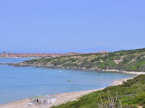 A coastal view with a beach, a small boat, and a building with a flag.