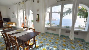 A dining area with a table and chairs, a TV, and a view of the sea through large windows.
