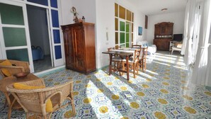 A room with a patterned floor, a dining table with chairs, a wooden cabinet, and a television.