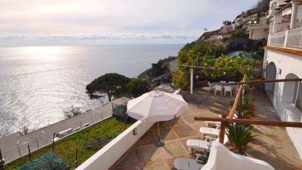 A terrace with a view of the sea, outdoor seating, and a pergola with plants.