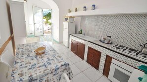 A compact kitchen with a dining area, white tiled floors, and a view through an open door to an outdoor patio.