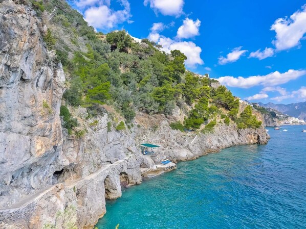 A coastal cliff with a narrow road leading to a small building.