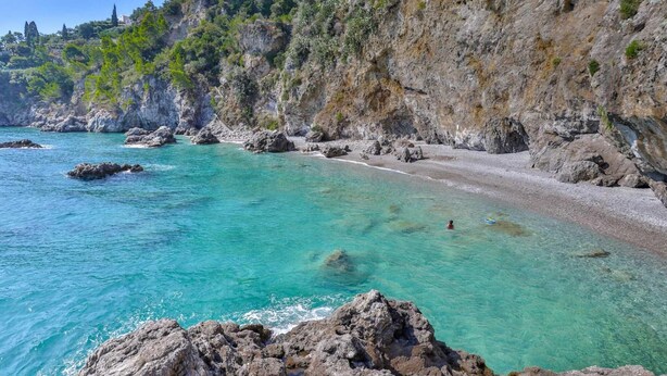 Un paysage côtier caractérisé par une eau turquoise et limpide, des falaises rocheuses et un bâtiment situé sur une colline.