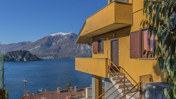 A yellow building with a staircase leading to a balcony overlooking a lake and mountains.