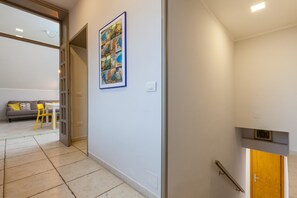 A hallway with a framed picture of Capri, a grey sofa with yellow cushions, and a yellow chair.