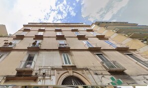 A multi-story building with balconies, a central entrance, and a clear sky above. - Bright Rooftop at CVE (Naples)
