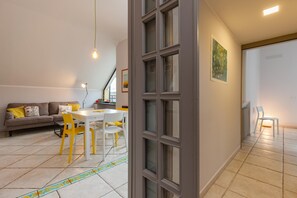 A modern living room with a sofa, a dining table with chairs, and a kitchen area visible through an open door. - Bright Rooftop at CVE (Naples)