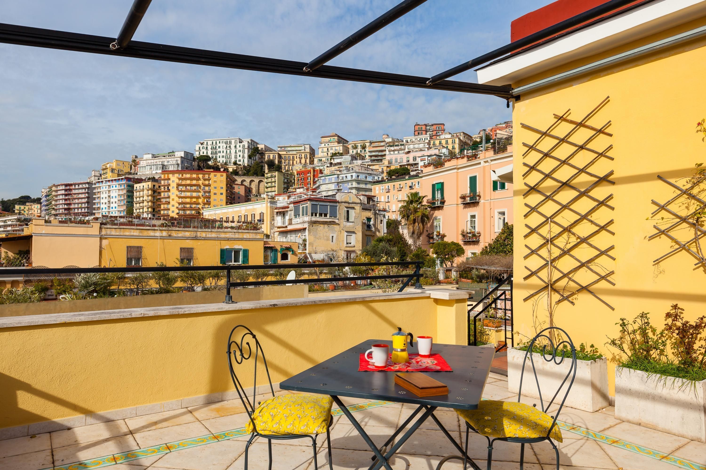Una terraza con una mesa y sillas, con vista a una zona urbana densamente poblada y varios edificios.
