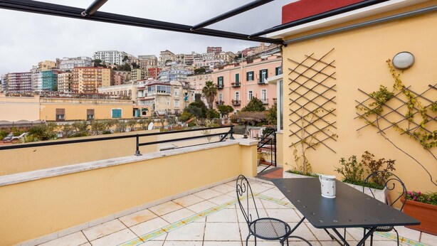 Un balcón con mesa y sillas, con vistas a un paisaje urbano con diversos edificios.