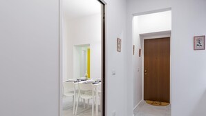 Un couloir mène à une salle à manger où se trouvent des chaises blanches et une table dressée pour deux personnes.