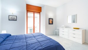 Une chambre avec un grand lit, une commode blanche et une porte donnant sur un balcon.