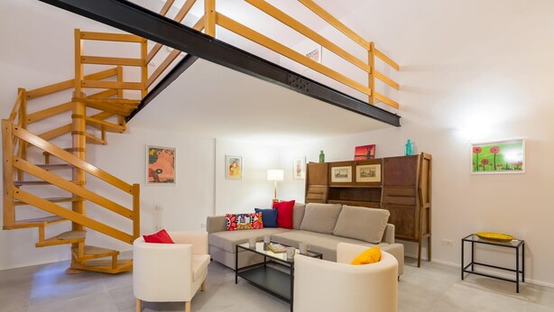 Un salon avec un escalier en bois, un ensemble de canapés, une table basse et une bibliothèque.