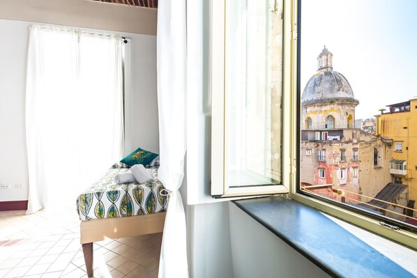 A room with a bed, a window with a view of historic buildings, and a curtain.