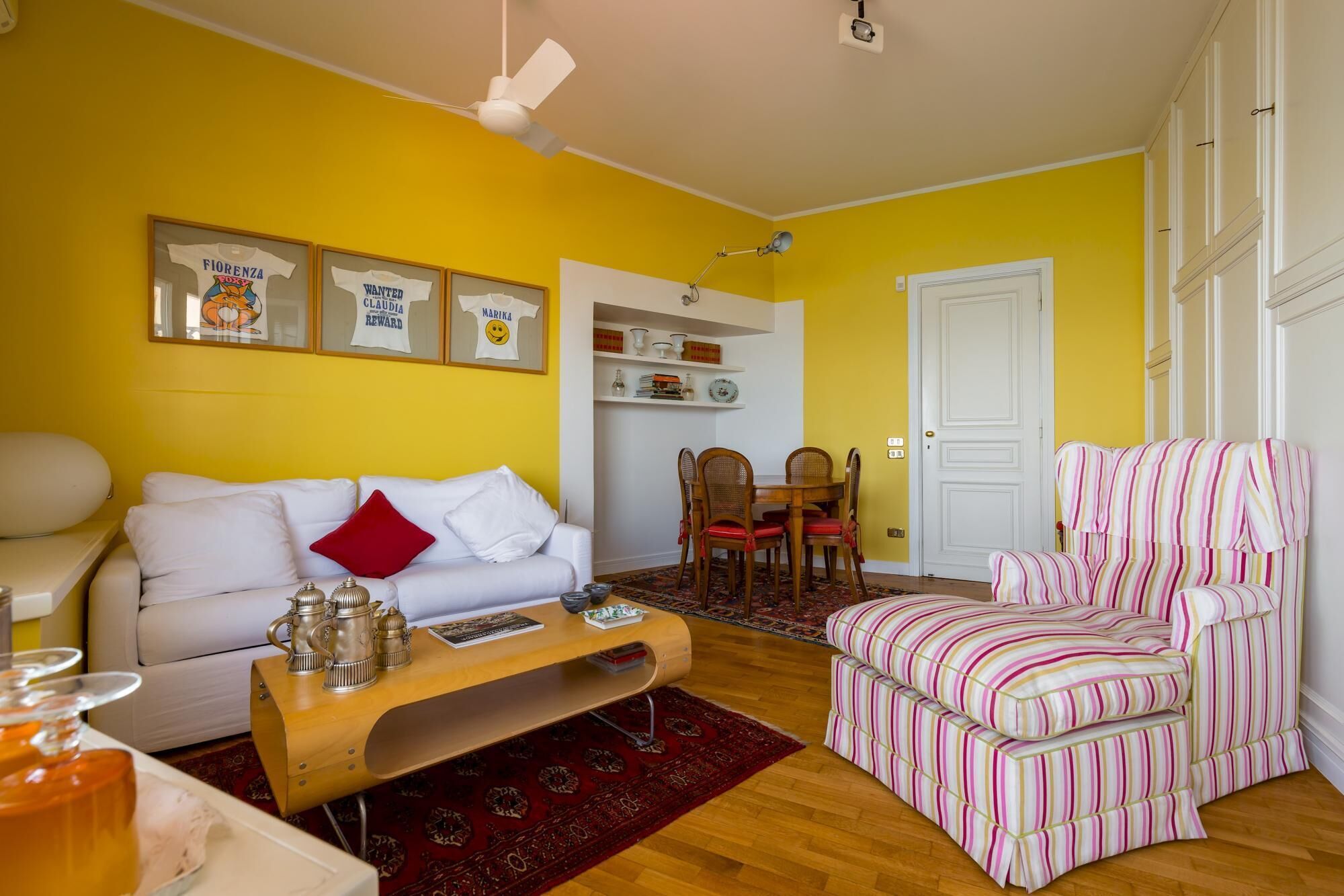 A living room with a white sofa, a wooden coffee table, a striped armchair, and a dining area with a white table and chairs.