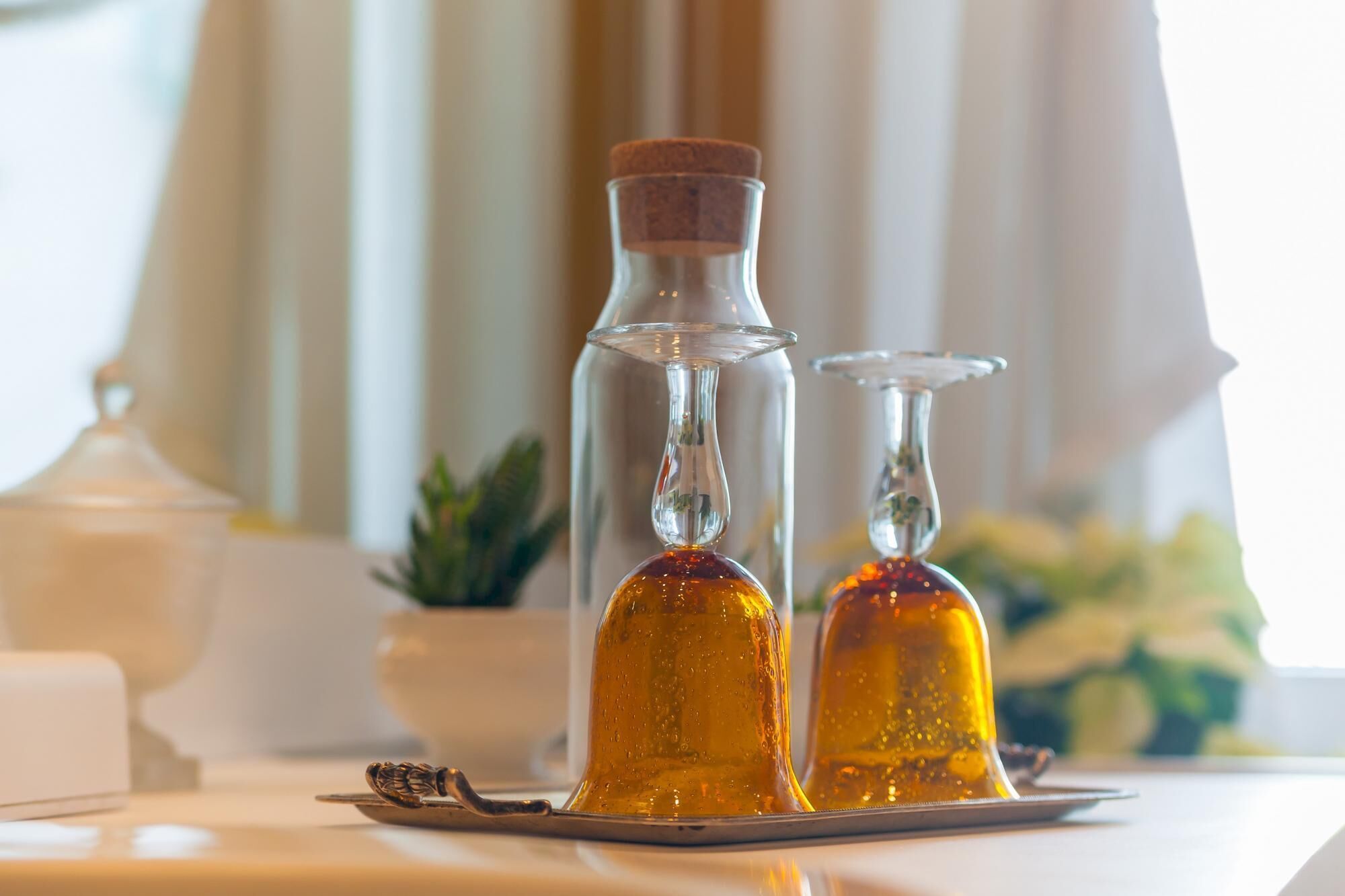 Two glass decanters with amber liquid on a tray, a white teapot, and a small plant in the background.