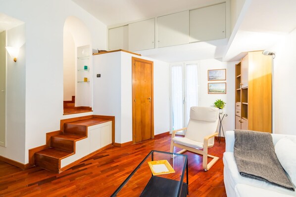 A spacious living area with a wooden staircase, a white sofa, a glass coffee table, and a chair. - Parthenope s Eye on the Seafront (Naples)