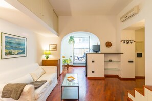 A modern living room with a sofa, a coffee table, and a TV. There is a dining area with a table and chairs visible through an archway. - Parthenope s Eye on the Seafront (Naples)