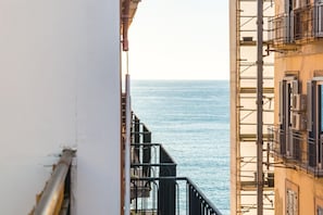 Uitzicht op zee vanaf een balkon met metalen hekwerk en een gevel op de achtergrond.