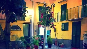 Pátio externo com vasos de plantas, uma fonte central e um edifício amarelo com sacadas.